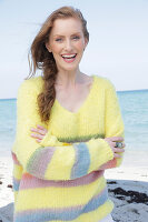 Young, blond woman in yellow jumper with coloured stripes by the sea