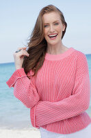 Good-humoured young blonde woman in a pink jumper by the sea