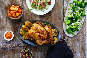 Grillhähnchen mit Kartoffeln, dazu Kumquats, Salat, Brokkoli und Oliven