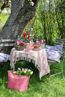 Garden table with spring flowers and bundt cake, tote bag with tulips in the grass