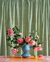 Roses in a blue vase in front of a green gingham curtain