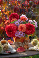 Herbstblumenstrauß aus Dahlien (Dahlia) und Astern, Kerzen in Schalen von Esskastanien (Castanea Sativa) und Herbstlaub