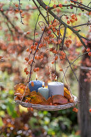 Candles with autumn leaves hanging in a basket from an ornamental apple tree