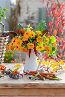 Autumn bouquet of marigolds (Calendula), nasturtiums (Tropaeolum), chard leaves and chillies on a patio table