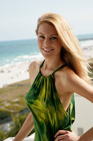 Blonde Frau in grünem Neckholder-Kleid am Meer