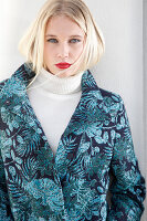 Young blonde woman in a white turtleneck sweater and transitional coat with leaf jacquard