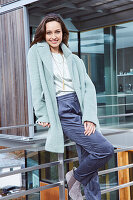 Young brunette woman in a silk blouse, blue trousers, and a light blue coat
