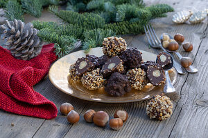 Weihnachtliche Deko mit Nüssen, Tannenzweigen, Pralinen auf goldenem Teller