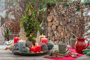 Weihnachtsdeko am Terrassentisch mit Kerzen, Kaffeetassen, Christbaumkugeln, Zapfen, Zimtstangen und Nüssen