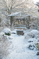 Verschneite Beete im winterlichen Garten und Pavillon mit Sitzplatz