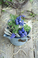 Eggshells filled with grape hyacinths (Muscari), daffodils and silver spoons in a rustic enamel pot