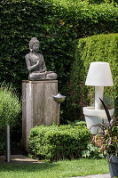 Buddha-Statue auf Holzsockel im Garten