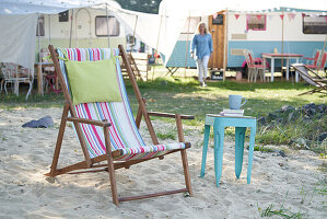 Deckchair in the sand in front of camper with small blue side table