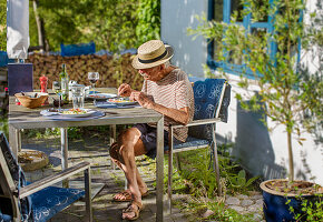 Älterer Mann beim Essen im Sommer vor einem Haus