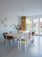 Dining room with large wooden table, assorted chairs and bouquet of flowers in front of glass doors