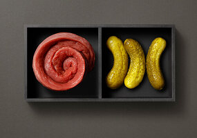 Tray with raw meat rolls and gherkins