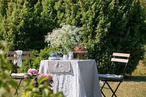 Gedeckter Tisch mit Blumen und Gugelhupf im sommerlichen Garten