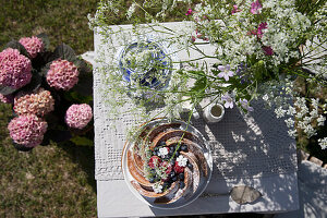 Gedeckter Tisch mit Blumen und Gugelhupf im sommerlichen Garten