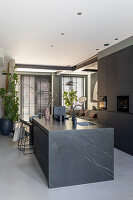 Modern kitchen with black marble island and black cupboards, seating area in the background