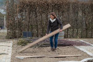 Frau bei Anlage eines Gemüsebeets mit Holzbrettern und Weidenzweigen als Rankhilfe für Kletterpflanzen