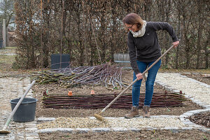 Frau bei Anlegen eines Gemüsebeets mit Flechtwand aus Weidenzweigen und Weg anlegen mit Kies