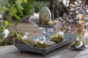 Pedestal with golden Easter eggs and quail eggs, feathers and moss, bunny figurines, Easter decoration