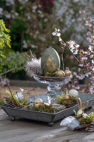 Pedestal with golden Easter eggs and quail eggs, feathers and moss, Easter decoration