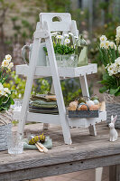 Daffodil 'Bridal Crown', daisies (Bellis) and primroses (Primula) in pots on an etagere with colored Easter eggs on metal tray, bunny figures