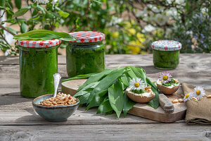 Make your own wild garlic pesto from wild garlic, pine nuts in a bowl, pesto in jars, egg, leaves on a chopping board, daisies as decoration