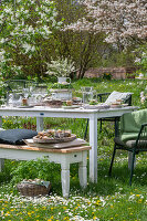 Gedeckter Tisch im Garten für Osterfrühstück mit Osternest und gefärbten Eiern in Eierbechern und Blumenstrauß in Etagere, Korb mit Eiern und Petersilie in Wiese