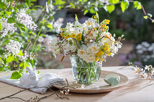 Blumenstrauß aus Schlüsselblume (Primula veris), Felsenbirne (Amelanchier), Narzissen 'Bridal Crown' (Narcissus) in Glasvase und Eierschale auf Gartentisch