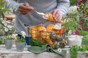 Blätterteigtüten im Ofen gebacken, mit Karotten-Dill-Sauresahnesoße befüllen, im Drahtkorb, gefärbte Ostereier, Gänseblümchen in Tassen als Vase