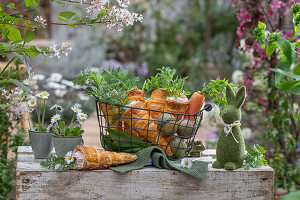 Puff pastry cones baked in the oven, filled with carrot and dill sour cream sauce in a wire basket and coloured eggs, herbs as decoration, daisies in a cup as a vase, Easter bunny figurine