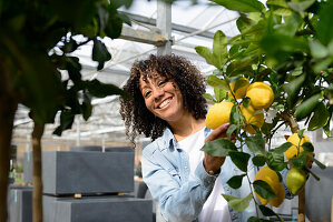 Lächelnde junge Frau in Gärtnerei an Zitronenbaum