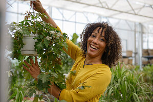 Lachende junge Frau in Gärtnerei hält Grünpflanze hoch