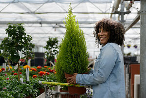 Smiling young woman in nursery with small tree in pot