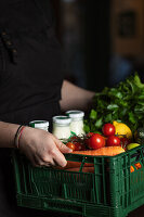 Frau hält eine Kiste mit Gemüse und Milch