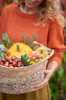 Frau hält Korb mit Zucchini, Kürbis, Äpfeln, Kastanien, Fenchelblüten und Mangold