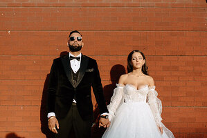 Portrait of bride and groom holding hands against brick wall