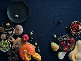 Herbstliche Lebensmittelzutaten auf dunkelblauem Hintergrund mit Kopierraum. Flat-Lay von Herbstgemüse, Beeren und Pilzen vom lokalen Markt. Vegane Zutaten