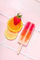 Frucht-Eis am Stiel mit Zutaten auf rosa Kachel-Hintergrund