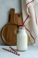 Raw cow milk in vintage closed bottle near drinking straws on gray surface against blurred napkin and cutting board