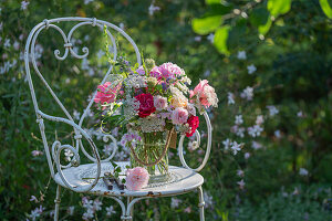 Bouquet of roses, wild carrot, flowering oregano, perennial vetch, autumn anemone and bearded flower on iron chair