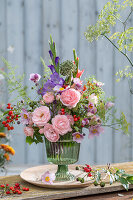 Colorful bouquet of roses (pink), gladioli, fennel blossoms, asparagus, rose hips, autumn anemone, onion blossom in glass vase