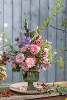 Colourful bouquet of roses (pink), gladioli, fennel blossoms, asparagus, rose hips, autumn anemone, onion blossom in glass vase