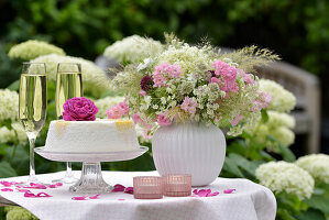 Bunter Wiesenblumenstrauß aus Sterndolden (Astrantia), Wiesenkerbel, auf einem festlich gedeckten Tisch mit Torte, Sektgläser und Rosenblüte