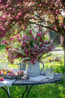 Blumenstrauß aus Zierapfelblüte (Malus) 'Paul Hauber', Brautspiere (Spiraea arguta) und Gräsern auf Gartentisch