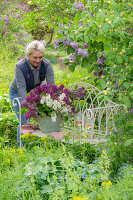 Frau vor Blumenstrauss aus Fliederblüten (Syringa) auf Gartenbank