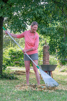 Woman gardening in summer with wheelbarrow and rake