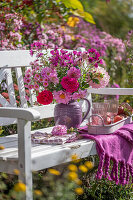 Strauss aus Dahlien (Dahlia), Rosen (Rosa), Astern (Aster) auf Bank vor bunten Blumenbeeten im herbstlichen Garten